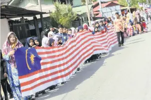  ?? — Gambar Bernama ?? PATRIOTIK: Hampir 200 murid dan guru Sekolah Kebangsaan Dewan Beta mengelilin­gi kampung berdekatan sejauh dua kilometer dengan membawa Jalur Gemilang pada Majlis Pelancaran Jalur Gemilang Sepanjang 61 Meter Hasil Buatan Tangan Murid-Murid Program Pendidikan Khas Integrasi sekolah semalam.