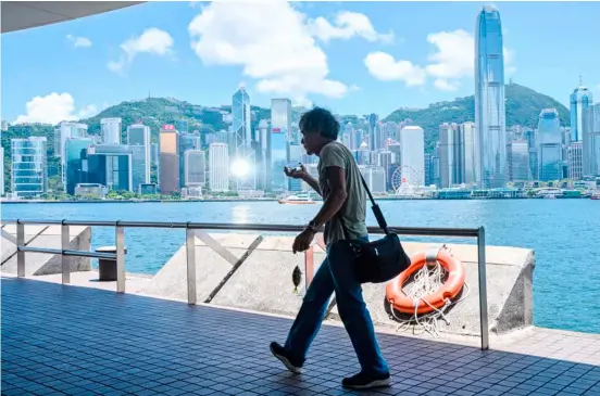  ?? ANTHONY WALLACE / AGENCE FRANCE-PRESSE ?? AN angler carries a fish on a hook as he walks along a promenade on the Kowloon side of Victoria Harbour, which faces the skyline of Hong Kong Island, in Hong Kong.