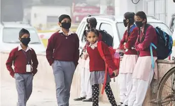  ?? PTI ?? Children wearing masks as protection against smog wait for their school bus in New Delhi yesterday. Schools in Delhi reopened yesterday following a four-day closure due to pollution.