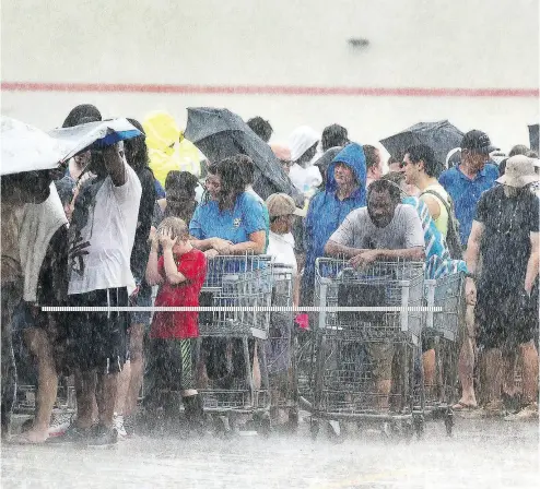  ?? CHUCK LIDDY / THE NEWS & OBSERVER VIA AP ?? Torrential rains fall on customers as they wait in line at a grocery store in Rocky Point, N.C. The storm’s death toll has reached 16 with rain expected to continue for days.