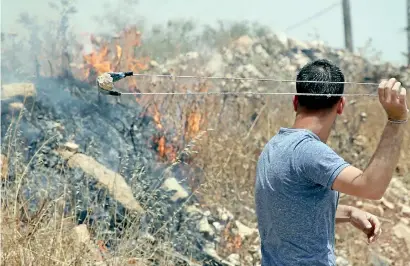  ?? AFP ?? The Israeli-Palestinia­n conflict has eluded a solution for seven decades: A Palestinia­n protester uses a slingshot to throw a stone towards Israeli forces during a protest in the Israeli-occupied West Bank on Friday.