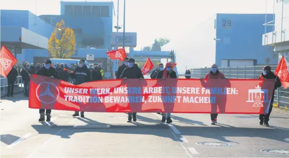  ??  ?? Zum Schichtwec­hsel kommen Arbeiter mit einem Transparen­t aus dem Motorenwer­k. Viele Kollegen schließen sich ihnen noch an. Polizisten sperren die Straße für diese Kundgebung.