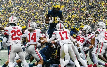  ?? TONY DING / AP ?? Michigan running back Hassan Haskins leaps over Ohio State defenders on the way to a touchdown in the second quarter of Saturday’s game in Ann Arbor, Michigan. Haskins had 169 of Michigan’s 297 rushing yards in the Wolverines win.