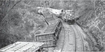  ?? JERRY JACKSON/BALTIMORE SUN ?? A freight train passes overturned rail cars near the Sisson Street bridge following an overnight derailment.