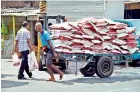  ??  ?? Above stocks of imported rice being transporte­d to the marketplac­e and below popular brands of rice being unloaded