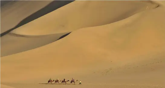  ?? (Reuters) ?? TOURISTS RIDE camels on the Mingsha Sand Dunes on the outskirts of Dunhuang.