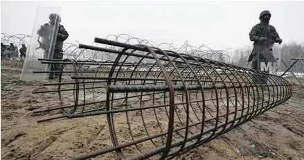  ?? Photo: AP ?? Guards and the military watching the start of work on the Guards and the military watching the start of work on the first part of a 180 kilometers (115 miles) and 5.5 meter (18ft)-high metal wall intended to block migrants from Belarus crossing illegally into EU territory, in Tolcze, near Kuznica, Poland.