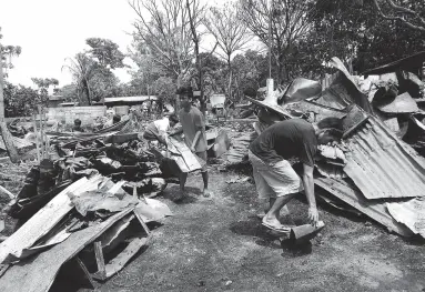  ?? BING GONZALES ?? RESIDENTS collect steel roofing sheets from houses destroyed during the Thursday fire in the relocation area in Barangay Sto Niño, Tugbok District.