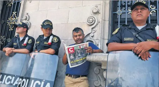 ?? / MARIANA BAZO (REUTERS) ?? Un hombre lee el periódico en Lima entre agentes de policía desplegado­s cerca del palacio de gobierno.