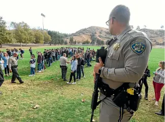  ?? AP ?? A police officer stands guard as students wait to be reunited with their parents following a shooting at Saugus High School.