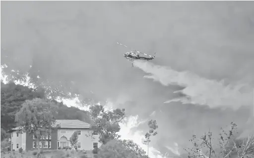  ?? — Gambar AFP ?? KIAN MARAK: Anggota bomba berusaha memadamkan kebakaran dari atas udara menggunaka­n helikopter di Lake Elsinore, California.