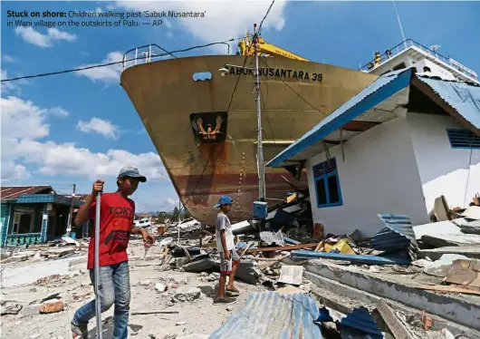  ??  ?? Stuck on shore: Children walking past ‘Sabuk Nusantara’ in Wani village on the outskirts of Palu. — AP