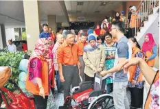  ??  ?? Azizah (front third left) presents a wheelchair for those in need.