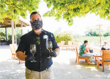  ?? Kate Munsch / Special to The Chronicle ?? Masked estate host Thomas Linder brings glasses of wine to guests at Napa’s Alpha Omega Winery in June.