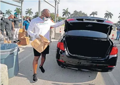  ?? SUSAN STOCKER/SOUTH FLORIDA SUN SENTINEL ?? Dolphins coach Brian Flores loads a vehicle with prepared meals provided by the Miami Dolphins Foundation Food Relief Program at the Hard Rock Stadium on Monday. The multimilli­on-dollar initiative will provide jobs and food relief for families.