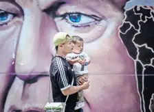  ??  ?? Un venezolano con un niño en brazos pasa en Caracas junto a una pared pintada con el rostro de Chávez, quien falleció de cáncer en 2013, en Cuba.