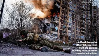  ?? EVGENIY MALOLETKA ?? > A Ukrainian police officer takes cover in front of a burning building hit in a Russian airstrike in Avdiivka