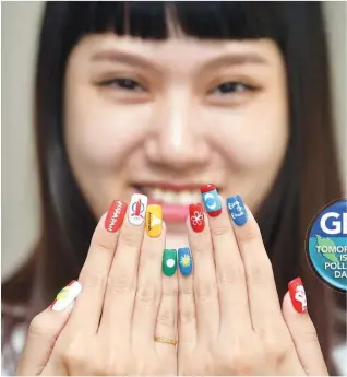  ?? BERNAMAPIX ?? ... Kmy Shin, 23, showing her finger nails painted with logos of political parties contesting the general election.