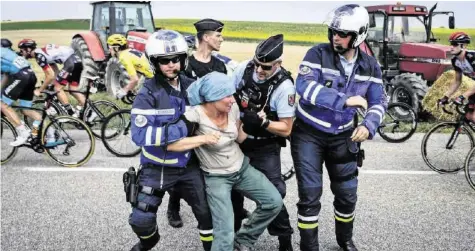  ?? AFP ?? Eine protestier­ende Bäuerin wird von der Polizei abgeführt, damit das Feld mit Leader Geraint Thomas (dahinter) passieren kann.