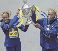  ?? STAFF PHOTO BY NANCY LANE ?? CHAMPIONS CELEBRATE: Boston Marathon women’s winner Edna Kiplagat (left) and men’s winner Geoffrey Kirui pose with the trophy at the finish line Monday.