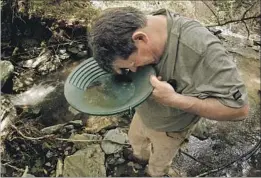  ??  ?? ROBERT GUARDIOLA uses a magnifying glass to look for gold in his pan. His personal claim is 20 miles south of Eagle Creek near the town of Moccasin.