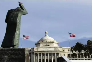  ?? RICARDO ARDUENGO AP ?? A bronze statue of San Juan Bautista stands in front of Puerto Rico’s capitol flanked by U.S. and Puerto Rican flags.