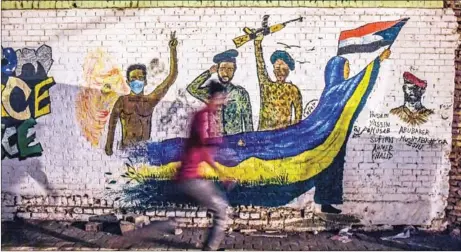  ?? OZAN KOSE/AFP ?? A Sudanese protester runs past a recently painted mural during a demonstrat­ion near the army headquarte­rs in the capital Khartoum in April.