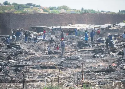  ?? Picture: Jacques Nelles ?? ALL LOST. Residents among the burnt down shacks of the Plastic View 2 informal settlement near the Pretoria East Cemetery yesterday. The informal settlement caught fire early in the morning and more than 50 homes were destroyed in the blaze.