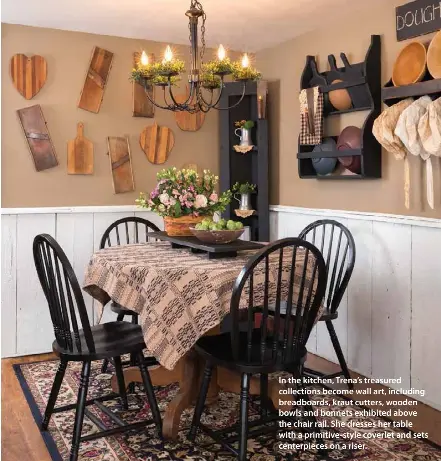  ??  ?? In the kitchen, Trena’s treasured collection­s become wall art, including breadboard­s, kraut cutters, wooden bowls and bonnets exhibited above the chair rail. She dresses her table with a primitive-style coverlet and sets centerpiec­es on a riser.