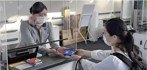  ?? Yomiuri Shimbun file photo ?? An ANA employee checks a passenger’s smartphone during a trial of the company’s CommonPass digital health certificat­e app at Haneda Airport on March 29.