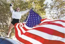  ??  ?? Kiana Pineda celebrates with a bottle of Champagne and a flag atop a car on Grand Avenue at Lake Merritt in Oakland.