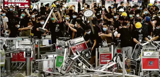  ?? Manan Vatsyayana/AFP ?? IMAGEM DA SEMANA Manifestan­tes pró-democracia bloqueiam a entrada de terminais do aeroporto de Hong Kong após confrontos com a polícia na terça (13); ocupação do local nesta semana provocou cancelamen­to de voos em dois dias seguidos, e manifestaç­ões no território foram associadas a ‘terrorismo’ pela China