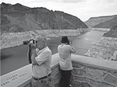  ?? JOHN LOCHER/AP ?? People take pictures of Lake Mead near Hoover Dam at the Lake Mead National Recreation Area on Aug. 13 in Arizona. The bathtub ring of light minerals shows the high-water mark of the reservoir, which has fallen to record lows.