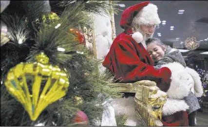  ??  ?? Santa Claus Barry Solomon, gets a big hug from Angie Lopez, 4, at the Ethel M Chocolate Factory. He said many children are asking for gifts for others rather than themselves this year. He lets them know he appreciate­s them.