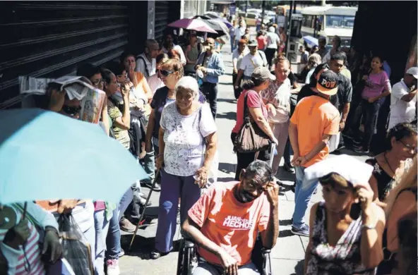  ??  ?? ► Un grupo de personas espera afuera de un supermerca­do para comprar alimentos básicos, el viernes en Caracas.
