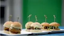  ??  ?? An array of burgers on slider buns ready for tasting on an outside picnic table.