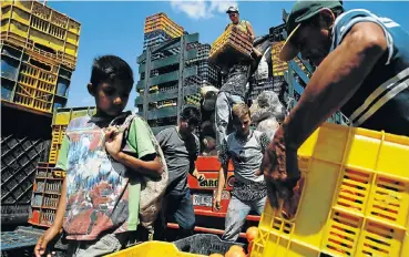  ?? Picture: Carlos Garcia Rawlins/Reuters ?? A child looks on while workers load merchandis­e into Humberto Aguilar’s truck at a market in Venezuela, which he will have to deliver to other markets at tremendous peril to himself on the country’s increasing­ly lawless roads.