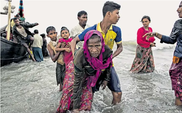  ??  ?? A young Rohingya man carries an elderly woman, after the wooden boat they were travelling on from Burma, crashed into the shore. An estimated 370,000 refugees have escaped Burma in the last three weeks