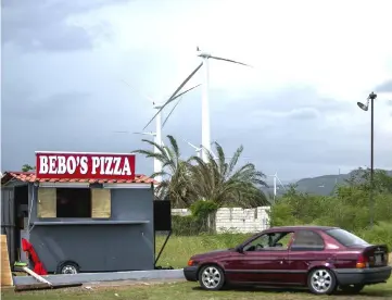  ?? WP-Bloomberg photo by Xavier Garcia. ?? A pizza shop stands in front of wind turbines in Barrio Jauca, Santa Isabel, Puerto Rico, on Oct 23, 2017.—