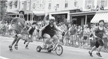  ?? KIM HAIRSTON/BALTIMORE SUN ?? Liz Baker of Hampden rides the SIlver Bullet as, team pushers, left to right, Laith Dashi; her son, Matthew Baker; and Aaron Chan run with her to the finish line in the first round of the Hampden Toilet Races during Hampdenfes­t.