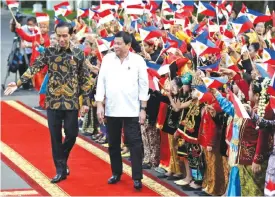  ??  ?? JAKARTA: Philippine President Rodrigo Duterte, right, walks with his Indonesian counterpar­t Joko Widodo as school children in traditiona­l dress wave the national flags of the two countries during a welcome ceremony at Merdeka Palace. — AP