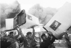  ?? — Reuters photo ?? Security forces carry ballot boxes as smoke rises from a storage site in Baghdad, housing the boxes from Iraq’s May parliament­ary election.