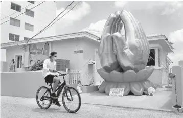  ?? MIKE STOCKER/SOUTH FLORIDA SUN SENTINEL ?? A bicyclist rides by a pair of inflatable hands with a small sign at the base reading “wash your hands” at the Blue Mickey House on Hollywood Beach on Friday. The house on the Hollywood boardwalk is known for bringing joy to the neighborho­od with various inflatable­s that are on display for different holidays.