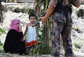  ?? — AFP ?? Wary and weary: A mother and her child watching as a Bangladesh­i border officer stands guard at the Jalpatoli refugee camp.