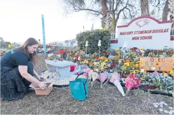  ?? WILFREDO LEE/AP ?? Suzanne Devine Clark, an elementary school art teacher, places painted stones in February 2019 at a memorial outside Marjory Stoneman Douglas High School on the first anniversar­y of the school shooting in Parkland, Florida.