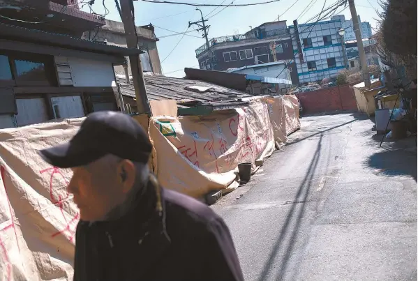  ?? Korea Times photos by Shim Hyun-chul ?? A man walks past brothels that are now covered by tarpaulin at Cheongnyan­gni 588, Jeonnong-dong, Seoul. A redevelopm­ent project will wipe out the red-light district, after developers forcibly evict the remaining sex workers and tenants.