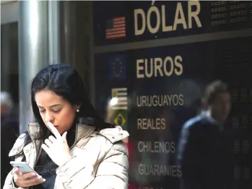  ??  ?? A woman looks at her cellphone as she stands in front of a currency exchange board in Buenos Aires’ financial district in Argentina. — Reuters photo