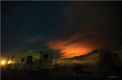  ?? DARRYL DYCK, THE CANADIAN PRESS ?? A shooting star streaks across the sky above a trailer parked at a campground in Savona, B.C., as the Elephant Hill wildfire burns in the distance near Clinton, illuminati­ng smoke in the sky during the early morning hours of Sunday.