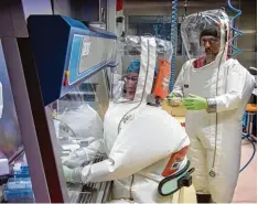  ?? Fotos: Soeren Stache/dpa ?? In die Anzüge wird Luft gepumpt – damit die Labormitar­beiter atmen können und da mit kein Virus von außen eindringen kann.