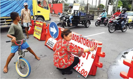  ?? DIPTA WAHYU/JAWA POS ?? TETAP BUKA: Ninik, petugas Klinik Biotest, memasang tulisan yang menunjukka­n bahwa tempatnya bekerja tetap buka seperti biasa kendati Jembatan Kartini ditutup. Hal yang sama dilakukan pemilik tempat usaha lain.